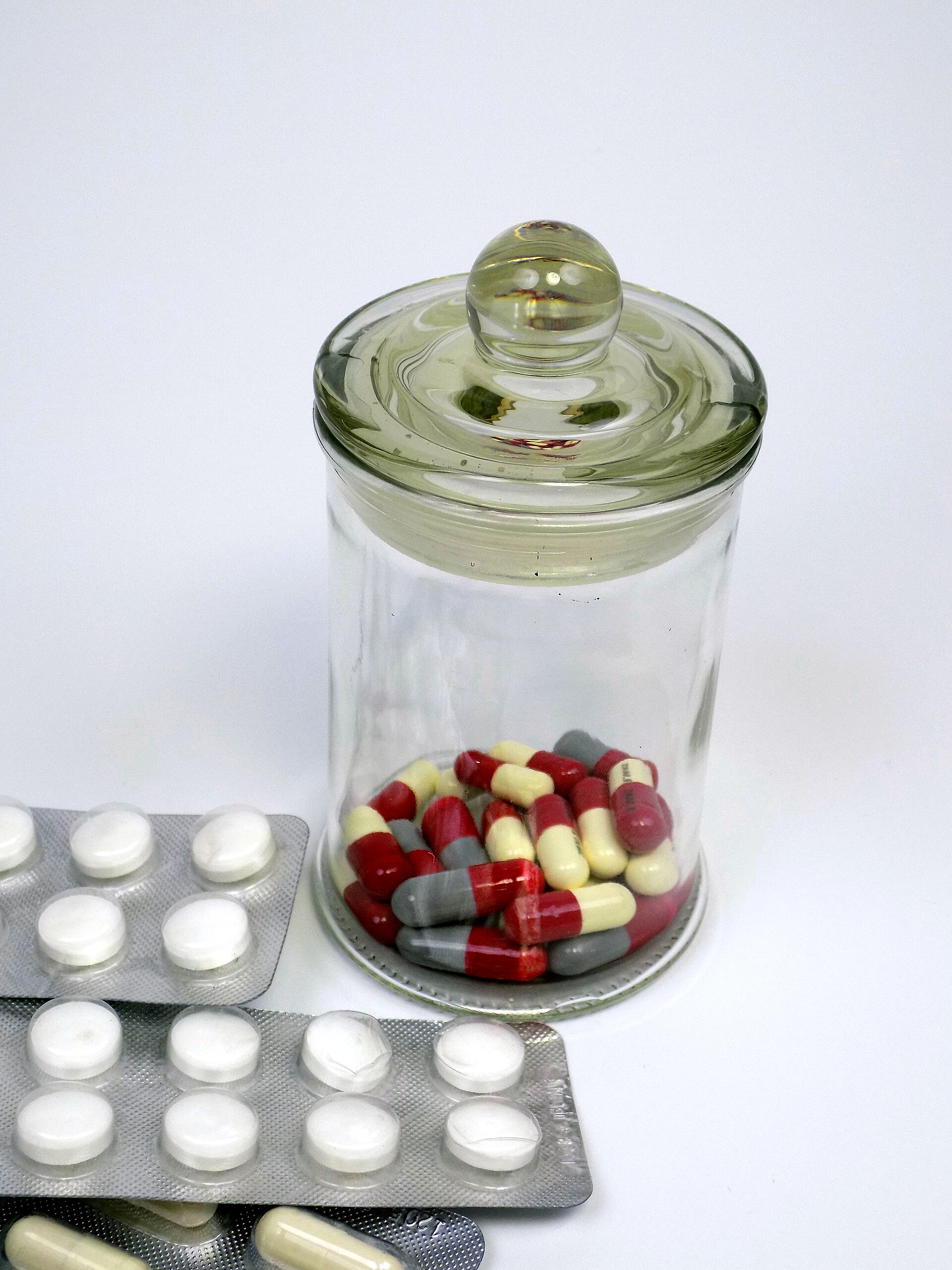 Hard-shell capsules in a clear glass jar beside blister packs of white tablets
